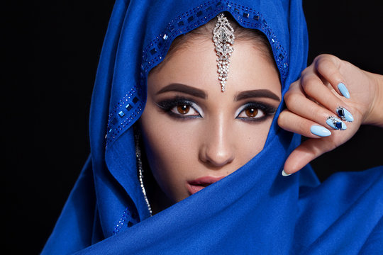 Gorgeous Young East Woman face portrait in hijab. Beauty Model Girl with bright eyebrows, perfect make-up, touching her face. Traditional. Isolated on black background. Smokey.Jewelry on her face