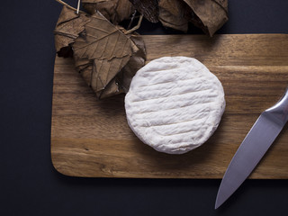 French banon cheese on wooden cutting board withs its chestnut leaves, isolated on black background