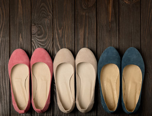 Women's shoes (ballerinas) pink, blue and beige on a dark wooden background.