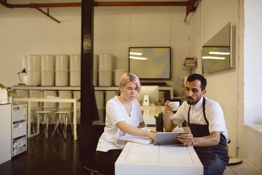 Male and female barista having coffee while using digital tablet