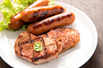 Grilled meat, sausages and vegetables on dish close up