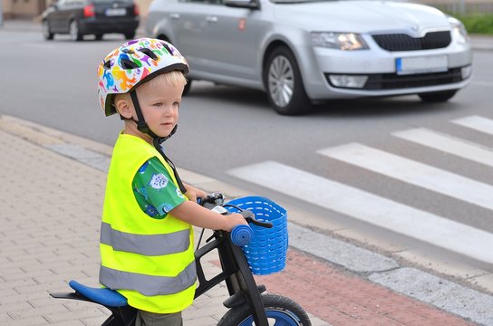 Little boy standing at a pedestrian crossing and looking around. Child must be careful. There is traffic.