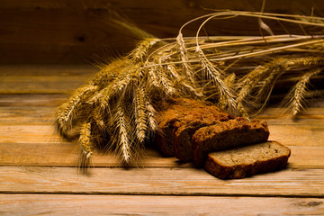 Rye bread, a loaf, ears of corn on a background of wooden boards, studio light