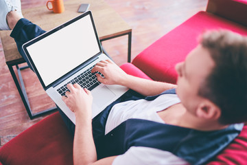 Copy space on the screen. Working at home. Young man using laptop computer while sitting on sofa.