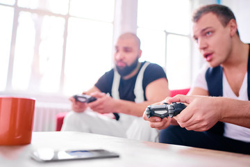 Friends and video games. Two handsome young men playing video games while sitting on sofa