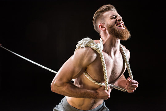 handsome bearded sportsman yelling and pulling rope isolated on black