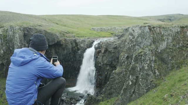 man taking photo of waterfall with his cell phone