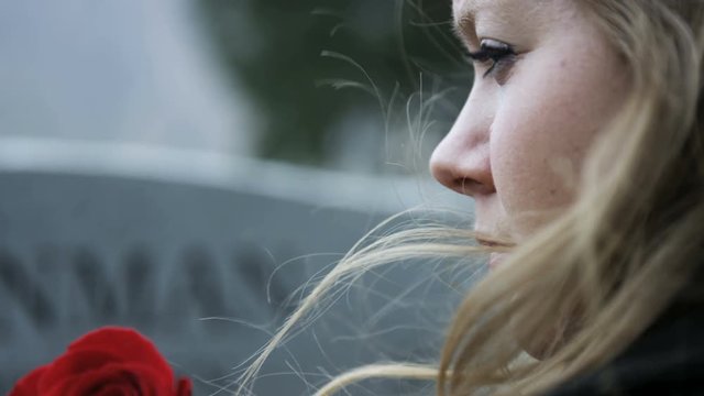 slow motion somber girl with rose visits gravestone in cemetery