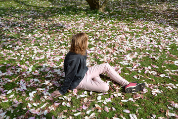 Mädchen sitzt auf einer Wiese voller Magnolienblüten   ( Magnoliaceae ) und schaut nach hinten