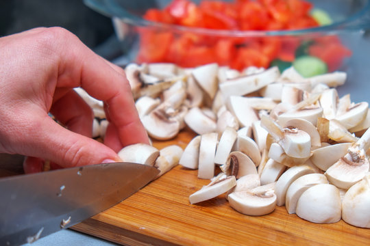 Сhef cutting mushrooms on wooden cutting board, prepares a salad