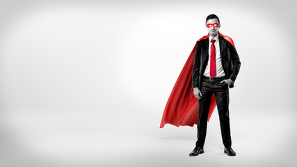 A self-assured businessman in a red cape and a mask standing with a hand in his pocket on white...