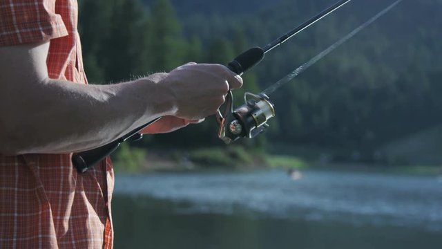 Man reeling in fishing line while fishing on a lake during the summer