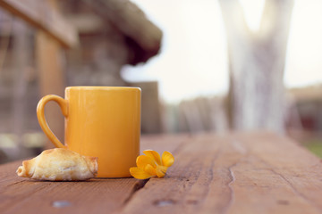 hot drink and dessert in the fresh air/ Croissant with a yellow mug and flower on a table on a background of a rural landscape