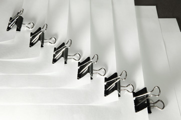 Black binder clips in a row clamping the paper close up white background