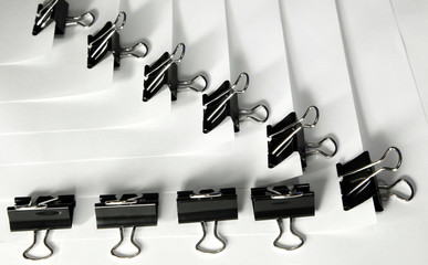 Black binder clips in a row clamping the paper close up white background