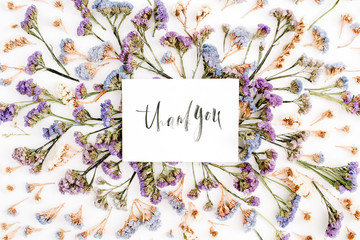 Words "Thank you" written in calligraphic style on paper with blue and purple dried flowers on white background. Flat lay, top view