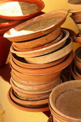 selection of terracotta plant and flower pots and dish saucers piled in a stack against a yellow wall