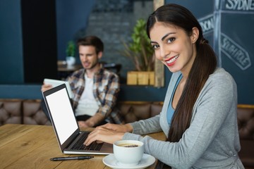 Portrait of young woman using laptop while having coffee