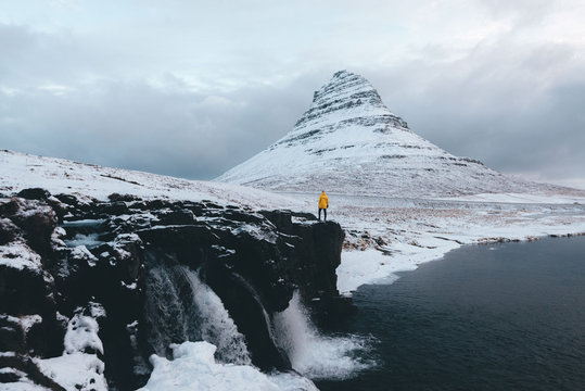 Person in yellow jacket standing in front of a mountain landscape with waterfalls in winter