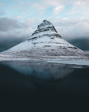 Reflection of Kirkjufell snowcapped mountain in lake against cloudy sky
