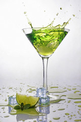 Splash in glass of green alcoholic cocktail drink with lime, mint and ice cube
