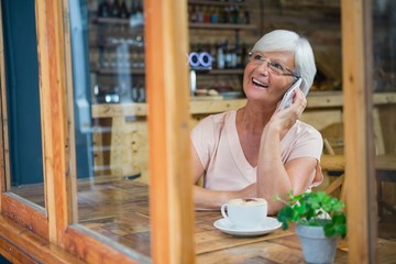 Senior woman talking on mobile phone while having coffee