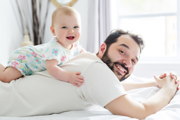 Fototapeta premium Young happy father playing with babyon bed