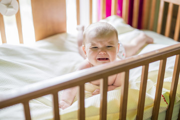 Close-up portrait of a crying cute baby in the crib at home