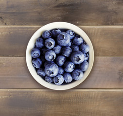 Blueberries in a white ceramic bowl. Top view. Ripe and tasty blueberries on a wooden background.