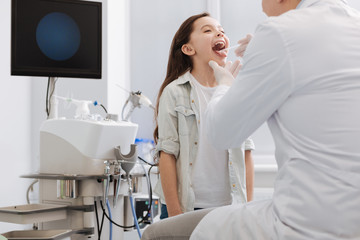 Competent doctor examining throat of little girl