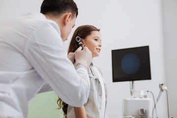 Competent pediatrician examining girls hearing