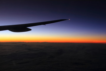 Fototapeta na wymiar Airplane wing in flight, warn and cold colors through from window, beautiful sunrise light