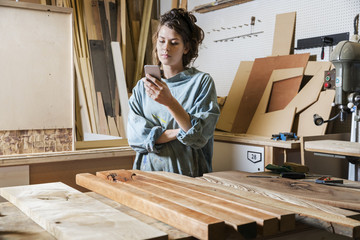 Young woman texting in a wood workshop