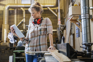 Woman consulting instructions on tablet while using machinery in wood workshop