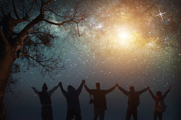 Milky Way.Night sky with stars and silhouette of standing happy peoples raised up arms.Blue milky way with people on the mountain.Background with universe.Night light landscape.Travel freedom concept.