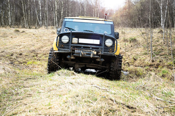 Obraz na płótnie Canvas The sport utility vehicle (SUV) is driving through the mud in the forest. The yellow car. Dirt, spring. Photo with lens flare