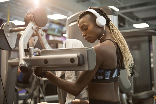 Young woman listening music while exercising on machine at gym