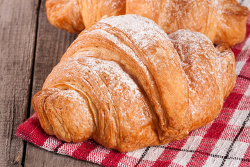 One croissant sprinkled with powdered sugar on a wooden table with napkin