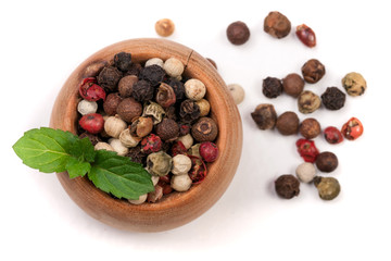 Mixture of peppers hot, red, black, white and green pepper in a wooden bowl isolated on white background. Top view