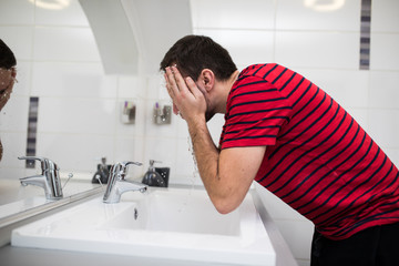 Handsome man washing face in bathroom in morning