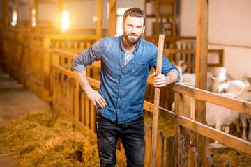 Portrait of a handsome farmer standing with fork at the goat barn. Natural milk production and...