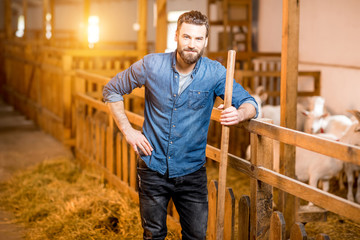 Portrait of a handsome farmer standing with fork at the goat barn. Natural milk production and farming