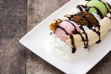 Banana split ice cream dessert with chocolate syrup on wooden background
