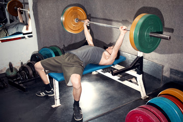 A young man performs bench press with a barbell.