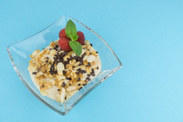 Eine Schale mit leckerem Dessert mit karamelisierten Mandeln, Schokostreuseln und frischen Himbeeren, blauer Hintergrund und Textfreiraum