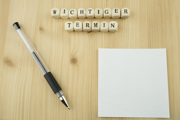 Weißer Zettel mit Textfreiraum, Holzbuchstaben mit den Worten wichtiger Termin, Holzhintergrund
