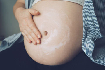 Pregnant woman putting cream on her belly to avoid stretch marks