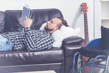 Charismatic invalid lying on the sofa and enjoying reading indoors
