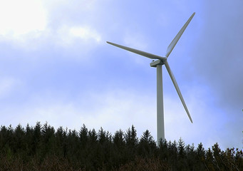 Wind turbine in forest on top of the hill with cloudy sky.