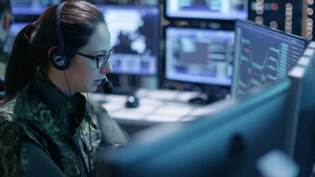 Female Military Technical Support Professional Gives Instructions into Headset. She's in a Monitoring Room with Many Working Screens.Shot on RED EPIC-W 8K Helium Cinema Camera.